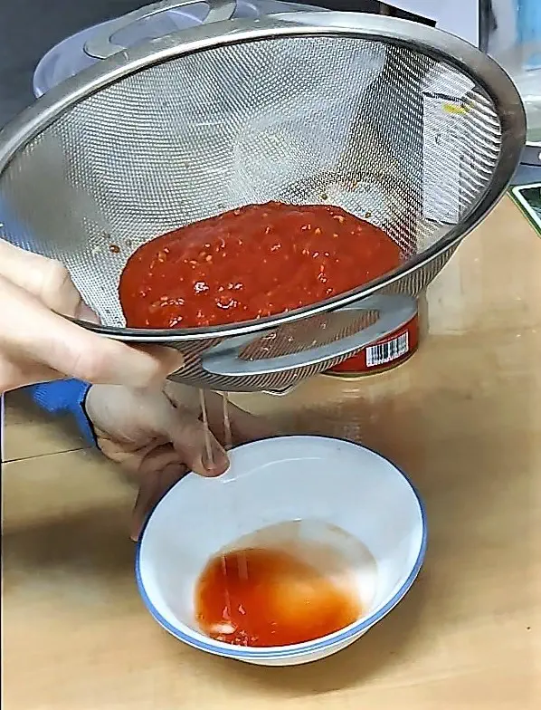 Straining pizza sauce with a sieve to thicken it