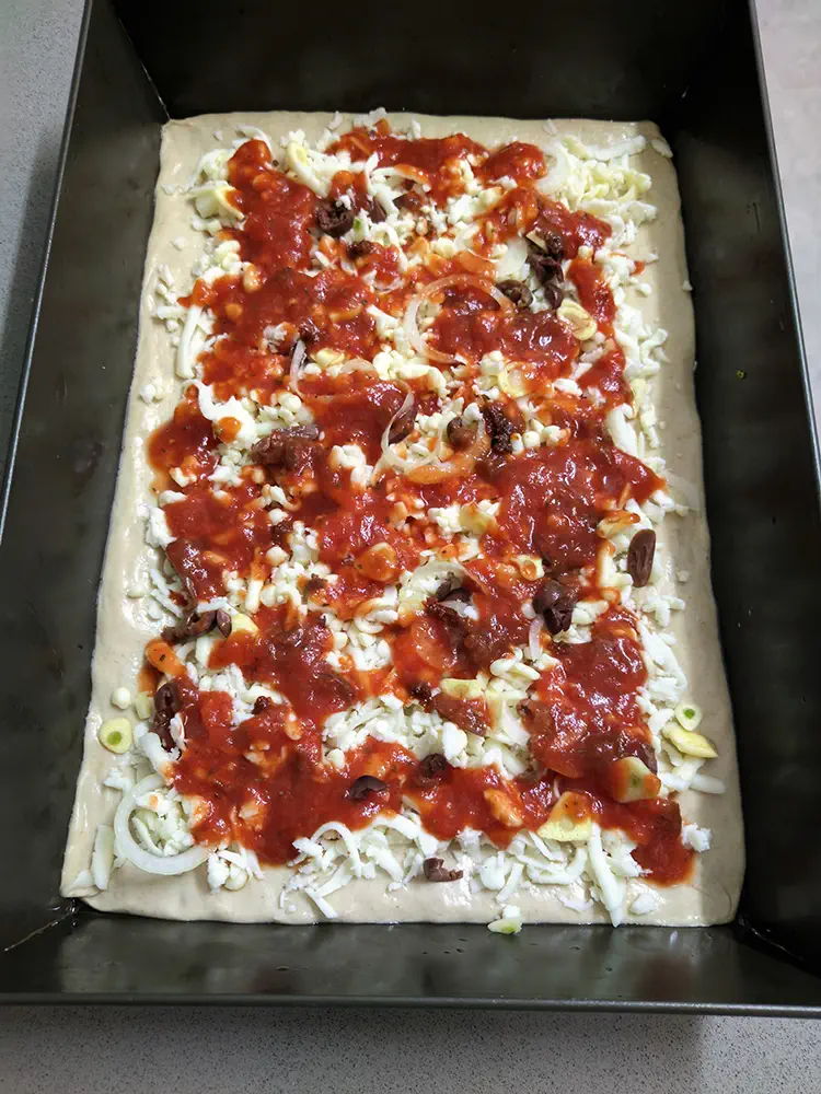 Grandma pizza with added sauce before baking